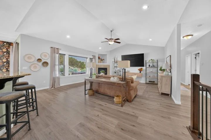 Vaulted ceilings with recessed lighting, wood-finish flooring, a fireplace with a stone surround, and a large picture window