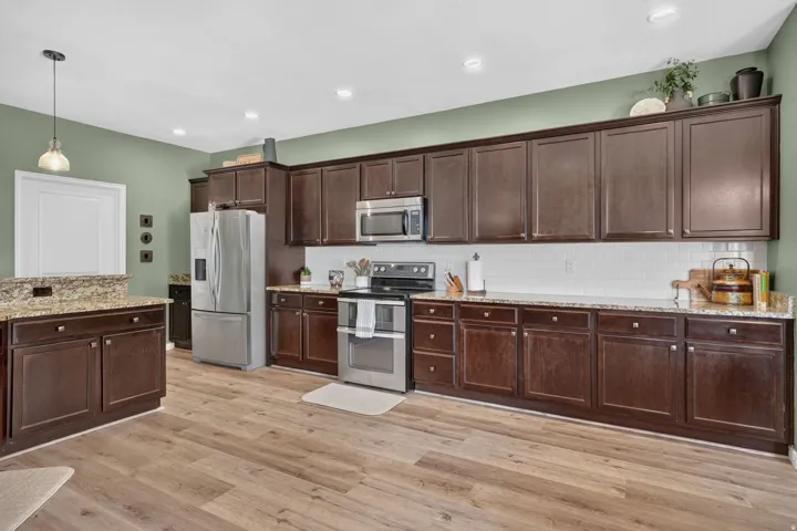 Spacious kitchen featuring extensive dark wood-finish cabinetry, light-toned wood-finish flooring, stainless steel appliances, granite-look countertops, and a subway tile backsplash