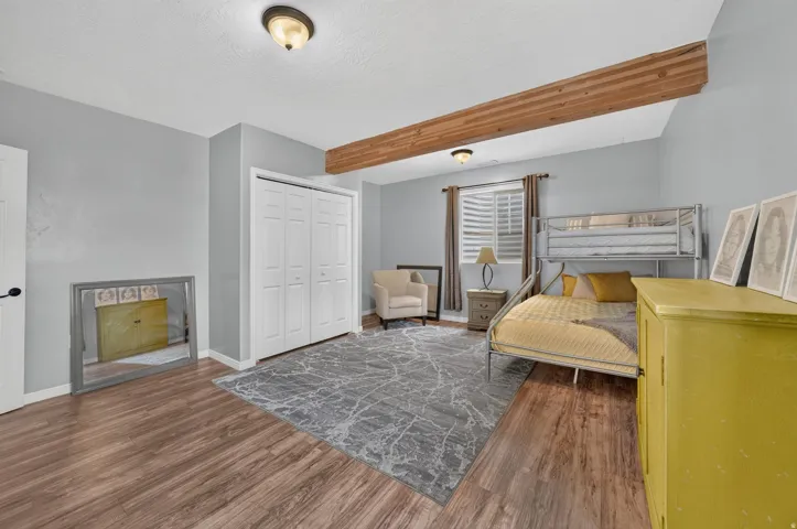 Wood-finish flooring, white bi-fold closet doors, exposed wood beam, recessed window with blinds, and flush-mount lighting