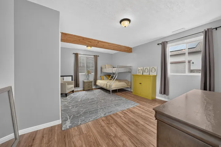 Wood-finish flooring, exposed wood beam, recessed window with blinds, and ceiling-mounted light fixtures
