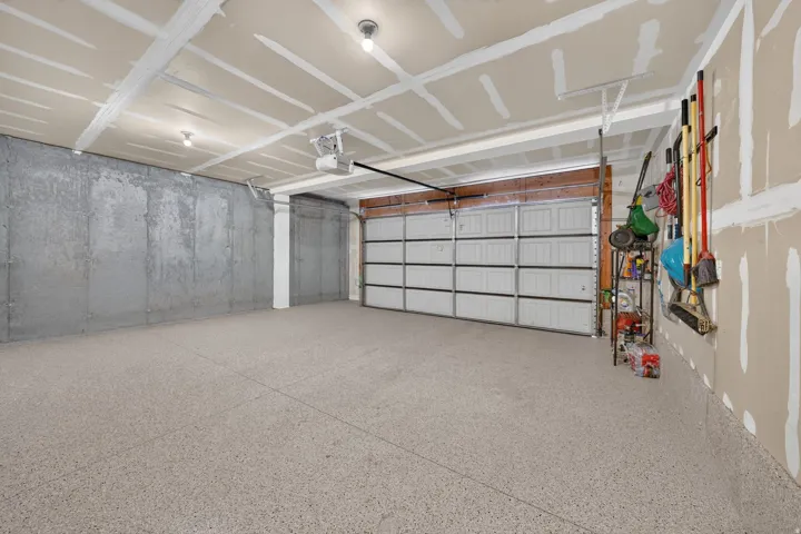 Spacious garage featuring a durable speckled epoxy floor, overhead lighting, an automatic garage door opener, and unfinished walls