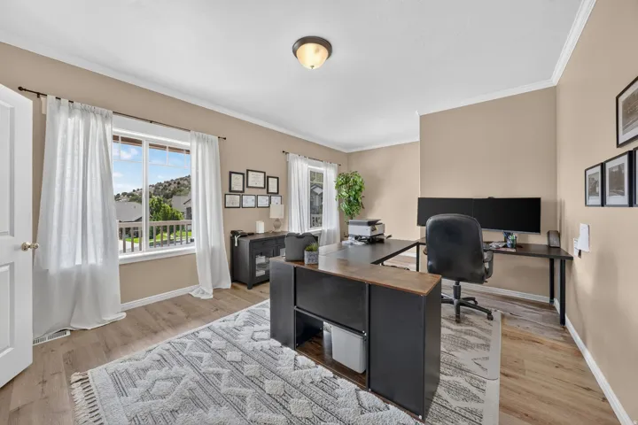 Spacious room with wood-finish flooring, two large windows, neutral wall paint, and crown molding