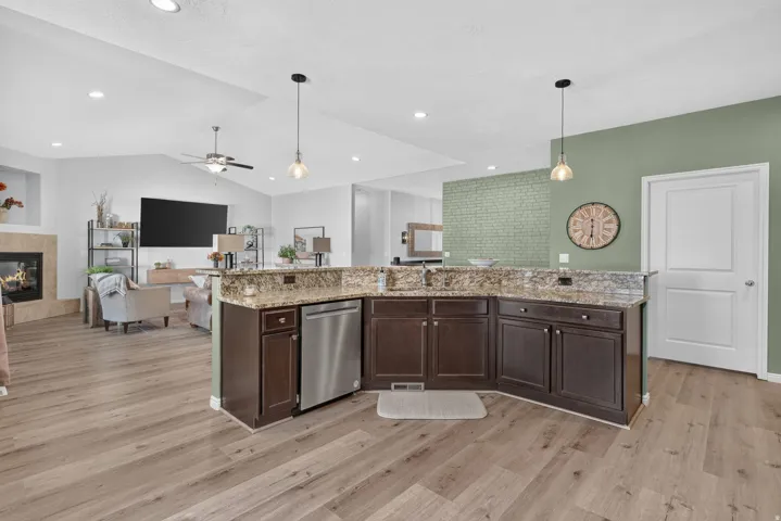 Spacious kitchen island with built-in stainless steel dishwasher, wood-finish flooring, recessed lighting, and vaulted ceiling