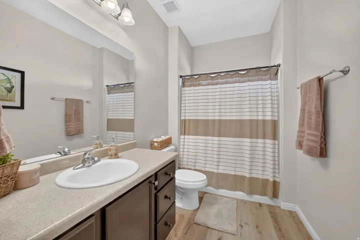 Bathroom featuring a single vanity, wood-finish flooring, a full-size mirror, and an integrated shower/tub