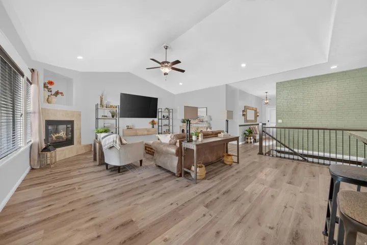 Vaulted ceiling featuring a ceiling fan, wood-finish flooring, a fireplace with a stone surround, and a wrought iron railing