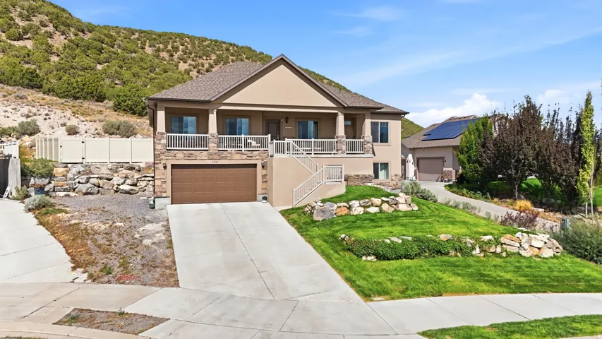 Stucco and stone exterior with a two-car garage, mature landscaping, and a covered balcony