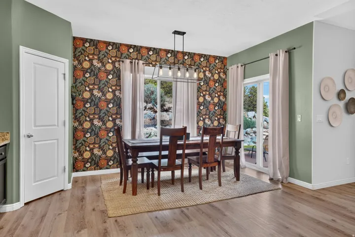 Wood-finish flooring, accent wall with patterned wallpaper, pendant lighting fixture, and sliding glass doors