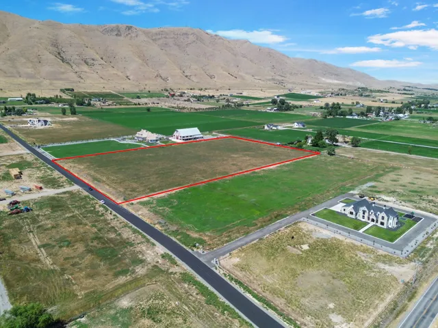 Expansive undeveloped lot featuring a grass expanse, paved road frontage, and a mountain backdrop