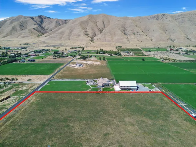 Expansive parcel with a mountainous backdrop, featuring a primary residence, an auxiliary structure, and a large open field