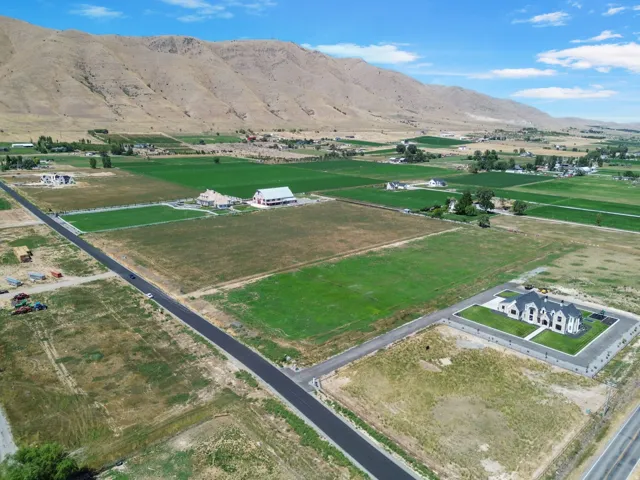 Expansive property featuring a developed lot with a landscaped yard, a substantial residence, surrounding agricultural fields, and a distant mountain backdrop