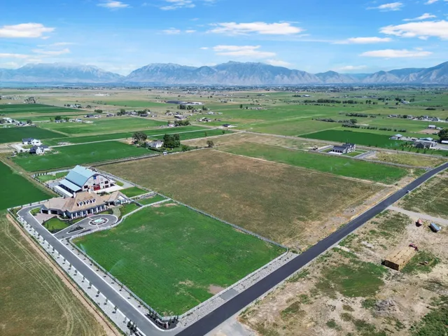 Expansive land parcel featuring a paved road, mountain backdrop, and surrounding agricultural areas