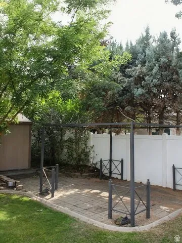 Paver patio area, metal pergola structure, privacy fencing, mature trees, and a storage shed