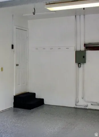 White walls, concrete flooring with a speckled finish, a utility door, and a built-in wall-mounted coat rack