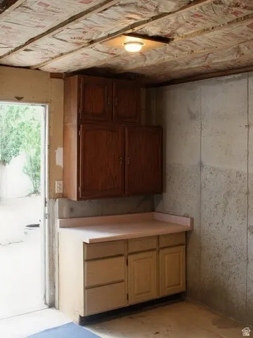 Built-in cabinetry with wood-finish doors and drawers, a light-toned countertop, and concrete walls