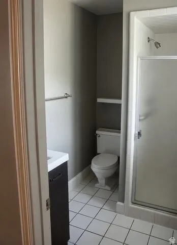 Bathroom featuring white square tile flooring, a dark wood-finish vanity with a white countertop, and a shower with a frosted glass door