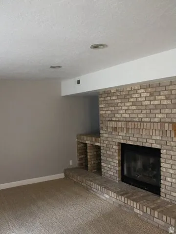 Brick-clad fireplace with hearth, built-in shelving, and carpeted flooring