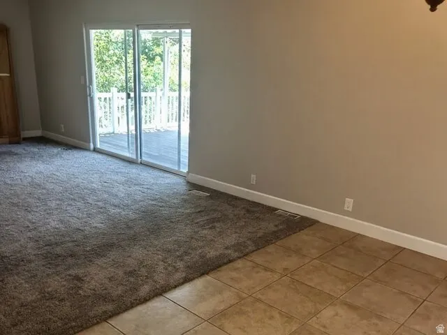 Sliding glass doors opening to an exterior deck with white railings, complemented by mixed flooring of broadloom carpet and square tile