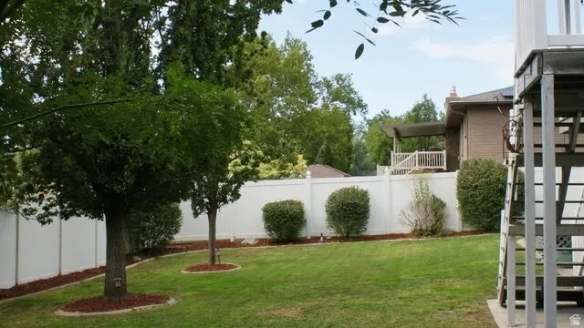 Expansive backyard with a manicured lawn, established trees, and a white privacy fence