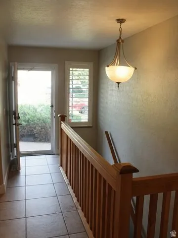 Tiled entry with wood railing, coordinating window shutters, and an overhead pendant light fixture