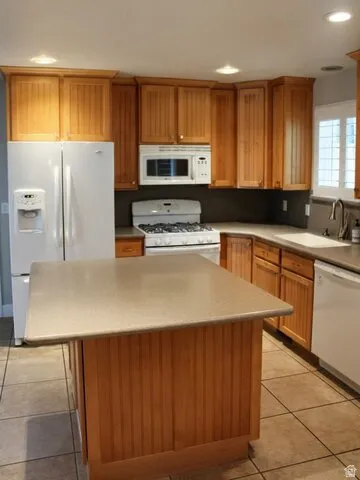 Kitchen featuring light wood cabinetry, a central island with a solid surface countertop, white appliances, and tiled flooring