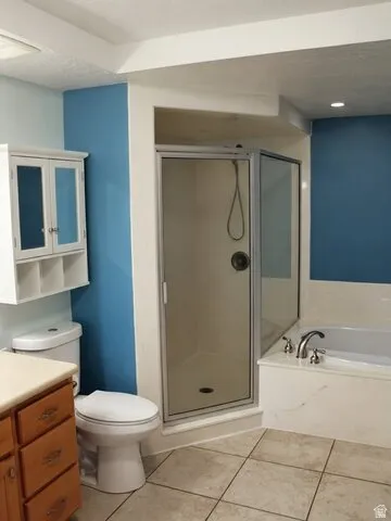 Shower enclosure with a glass door, a built-in bathtub, a toilet, a wood-finish vanity, and floor tiling