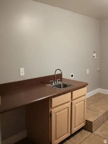 Utility area featuring a stainless steel sink, wood-finish cabinetry, and tiled flooring