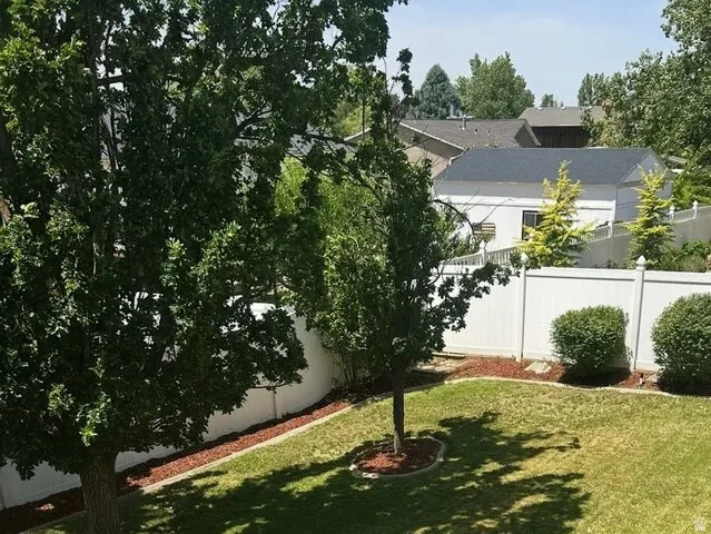 Spacious backyard featuring a manicured lawn, established trees, and a white privacy fence