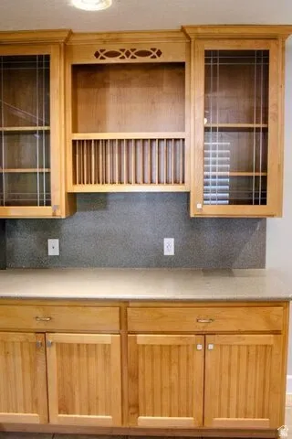 Light wood-finish cabinetry featuring glass-front doors, an integrated plate rack, and beadboard paneling