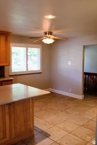 Kitchen featuring a wood-finish island with a light-toned countertop, tile flooring, and a ceiling fan with integrated lighting