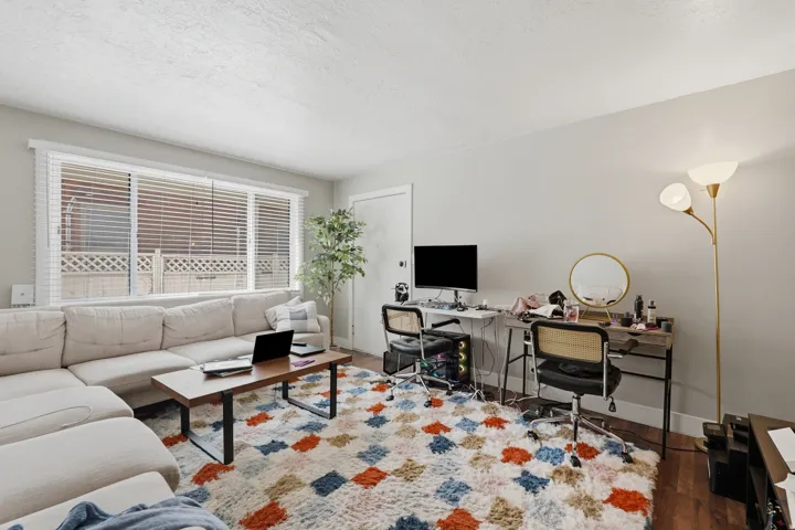 [Unit 2] Open living space featuring generous natural light through large picture windows, wood-look flooring, and ample room for versatile seating and workstation configurations.