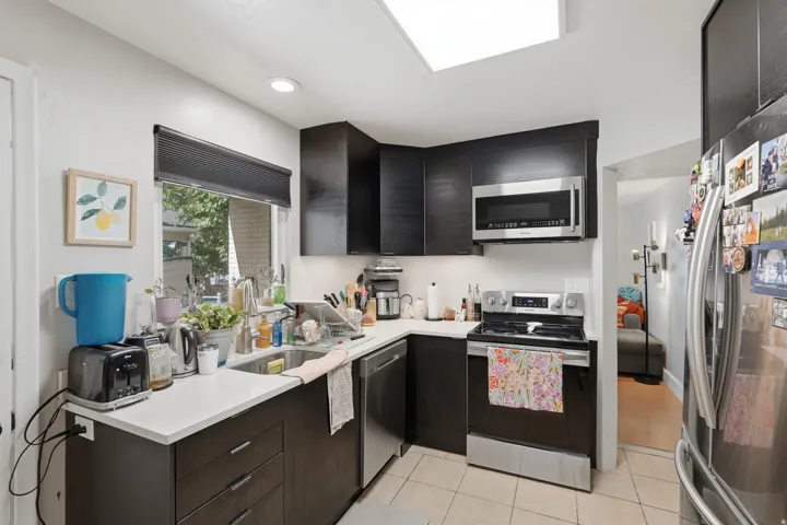 [Unit 1] Efficient modern kitchen equipped with stainless steel appliances, dark contemporary cabinetry, solid surface counter space, and tiled flooring.