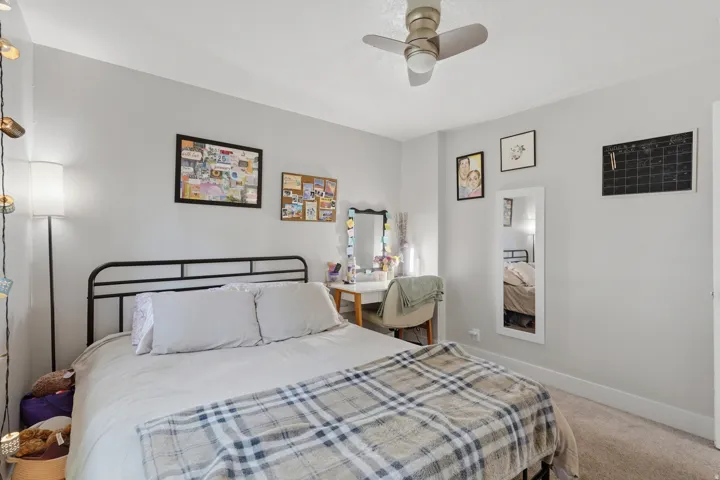 [Unit 1] Cozy bedroom featuring soft carpeting, an updated ceiling fan, and a large window providing ample natural light. The space comfortably accommodates a bed and a study desk.