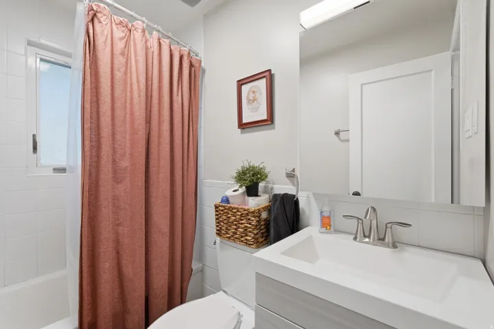 [Unit 1] Updated full bath featuring a modern floating vanity, crisp white tile surround, tub/shower combination, and natural privacy window light.