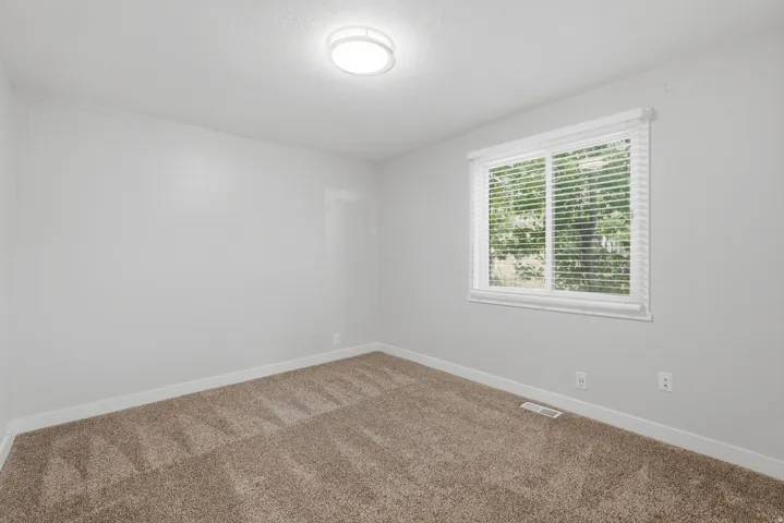 [Unit 3] Spacious bedroom featuring plush carpet, fresh wall paint, clean white baseboards, and a large window offering outdoor views.