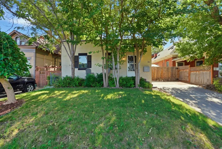 Inviting front elevation shaded by mature trees, complete with lawn space, decorative shutters, and private off-street driveway access.