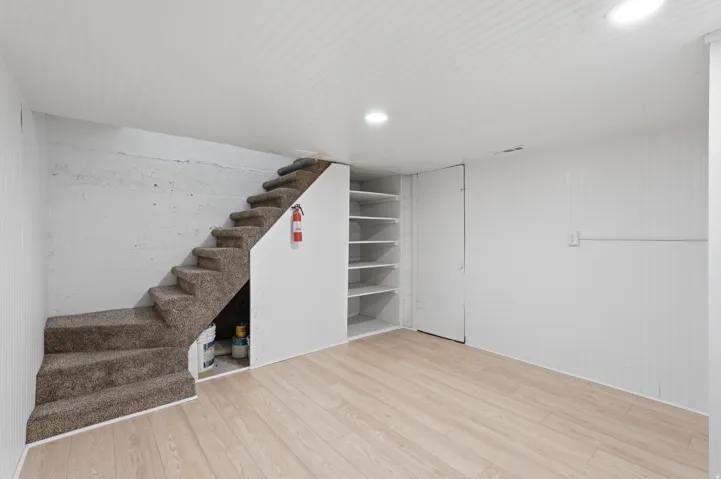 [Unit 3] Versatile lower-level flex space featuring wood-look flooring, recessed lighting, and integrated under-stair shelving and storage.