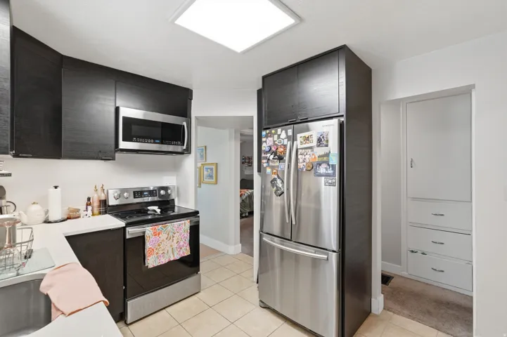 [Unit 1] Efficient modern kitchen equipped with stainless steel appliances, dark contemporary cabinetry, solid surface counter space, and tiled flooring.