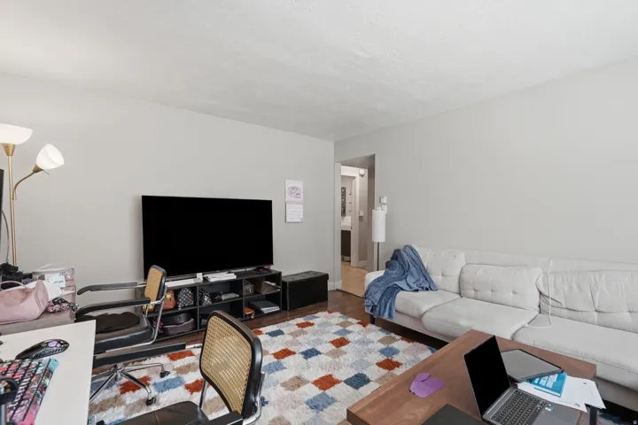 [Unit 2] Comfortable living area showcasing low-maintenance flooring, neutral wall paint, and direct connectivity to adjacent hallway spaces.