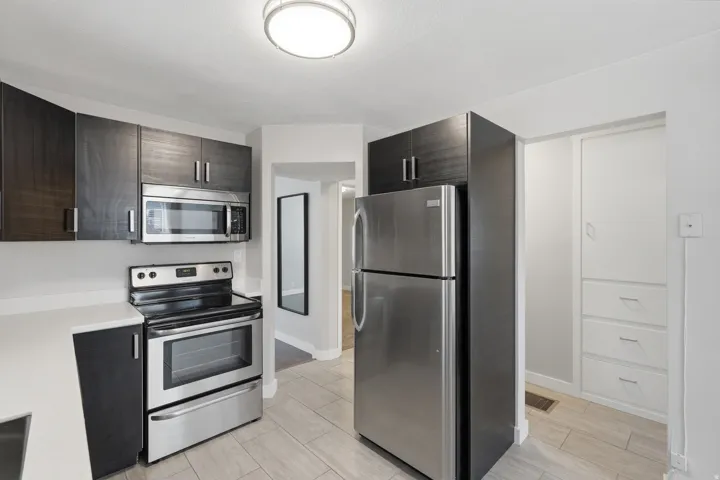 [Unit 3] Functional kitchen arrangement with rich espresso cabinetry, matching stainless steel appliance package, tile flooring, and direct exterior door access.
