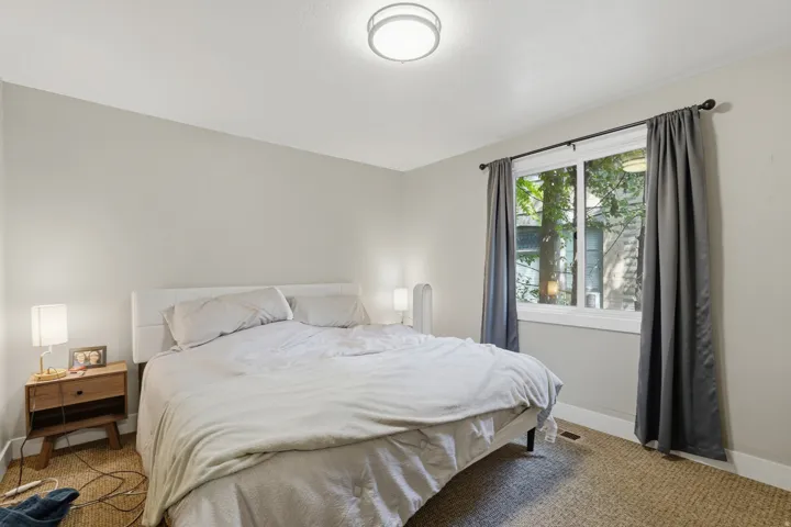 [Unit 2] Spacious primary bedroom offering natural lighting through a large window, neutral paint palette, and comfortable space for a king bed setup.