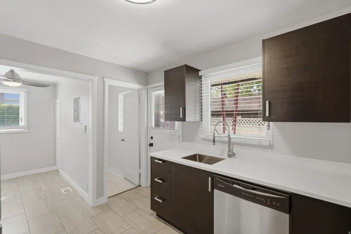 [Unit 3] Updated kitchen equipped with dark solid-wood cabinetry, white solid-surface countertops, under-mount stainless sink, and integrated dishwasher.