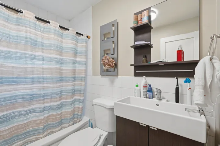 [Unit 2] Updated full bath boasting clean tile surround, modern dark-wood vanity with vessel-style sink, integrated shelving, and medicine cabinet.
