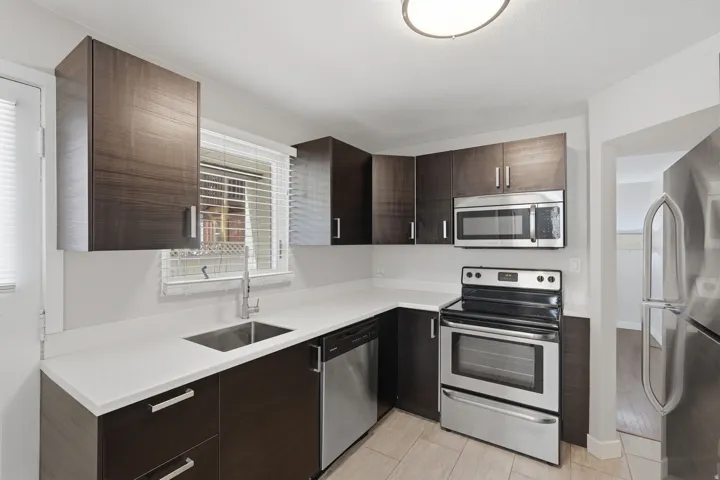 [Unit 3] Functional kitchen arrangement with rich espresso cabinetry, matching stainless steel appliance package, tile flooring, and direct exterior door access.