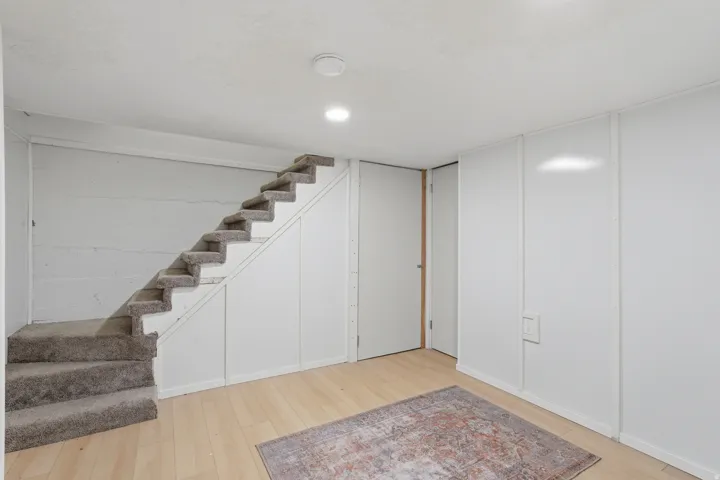[Unit 1] Versatile lower-level bonus area featuring wood-look flooring and built-in closet storage underneath the carpeted staircase. Perfect for a home office, gym, or rec room.
