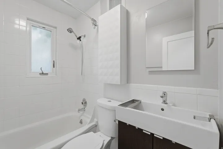 [Unit 3] Freshly updated bathroom boasting crisp white tile surround, modern vanity with dark cabinetry, floating medicine cabinet, and privacy window.