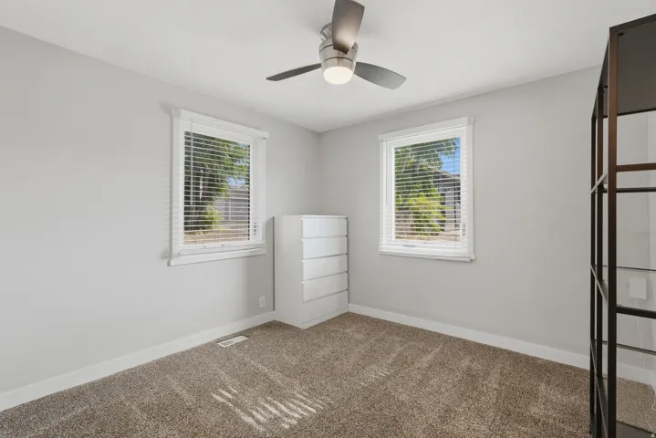 [Unit 3] Bright secondary bedroom featuring dual corner windows for maximum natural light, modern ceiling fan, and soft plush carpeting.