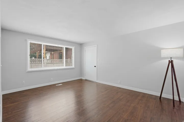 [Unit 3] Sunlit living room featuring warm wood-look laminate flooring, fresh neutral paint, and horizontal blinds.