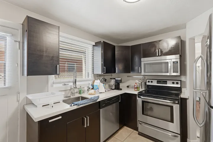 [Unit 2] Functional kitchen layout featuring solid-surface countertops, under-mount stainless sink with pull-down faucet, stainless dishwasher, and window over the sink.