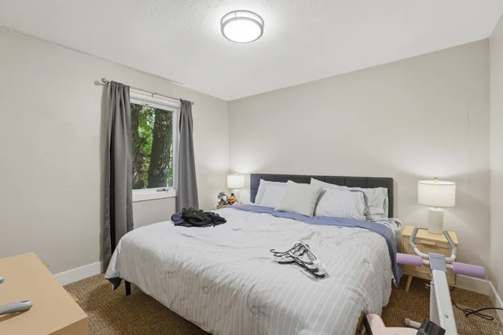[Unit 2] Cozy bedroom space with neutral walls, bright ceiling light fixture, and window overlooking lush greenery.