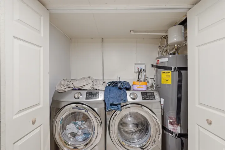 [Unit 2] Dedicated laundry space featuring front-loading stainless steel washer and dryer with closed bi-fold door storage and direct water heater access.